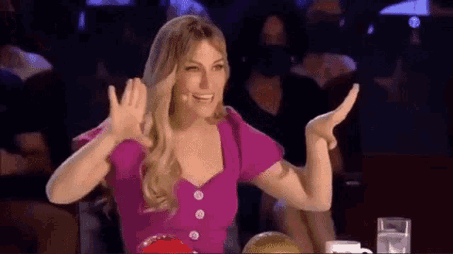a woman in a pink shirt is sitting at a table with her arms outstretched and smiling .