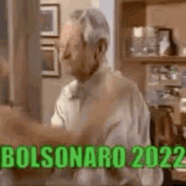 a man is sitting at a table in a room with the words bolsonaro 2022 written on the screen .