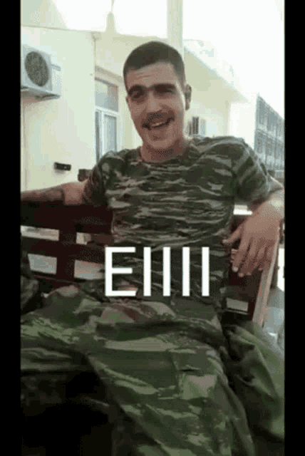 a man in a camo shirt is sitting on a bench with the word eiiii written on his shirt