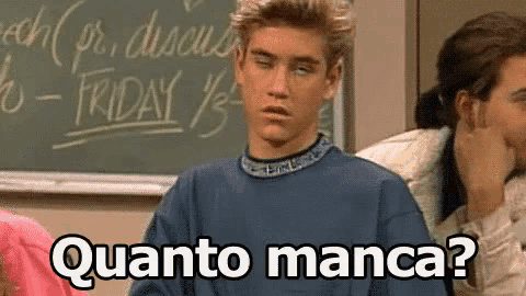 a man in a blue shirt is sitting in front of a blackboard and asking quanto manca ?