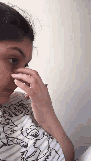 a woman is covering her nose with her hand while wearing a disney shirt .