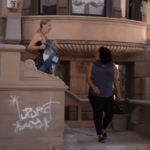 two women are walking down a set of stairs with graffiti on the side of a building that says upport