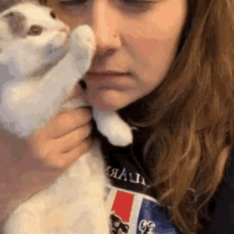 a woman is holding a white cat in her arms and the cat is touching her face .