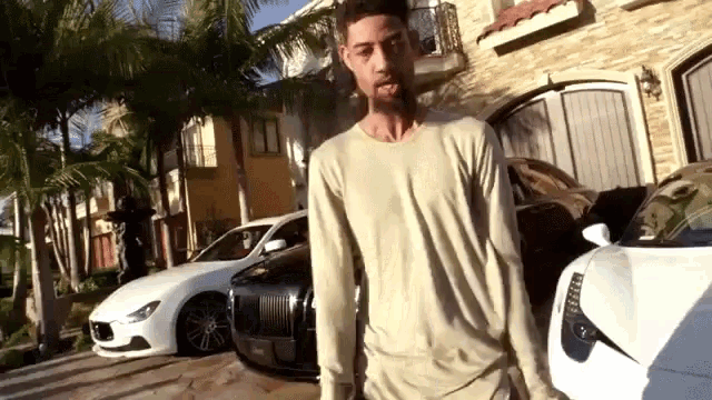 a man in a tan shirt stands in front of a row of white cars