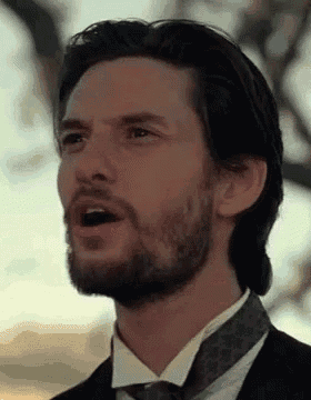 a man with a beard is wearing a suit and tie and making a funny face .