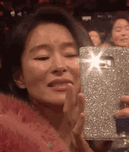 a woman is crying while taking a picture of herself with her phone .