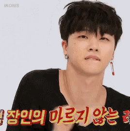 a young man wearing a black shirt and earrings is making a funny face in korean .