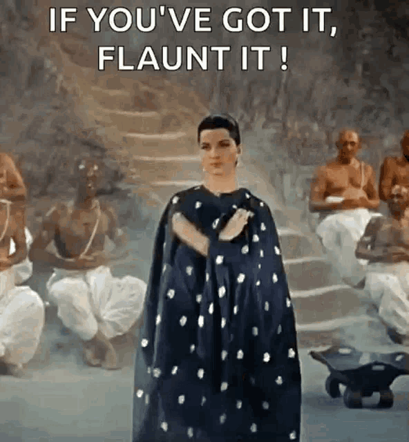 a woman in a cape is standing in front of a group of men with the words if you 've got it flaunt it !
