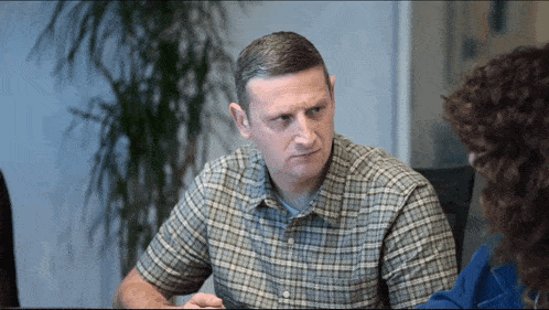 a man in a plaid shirt is sitting at a table