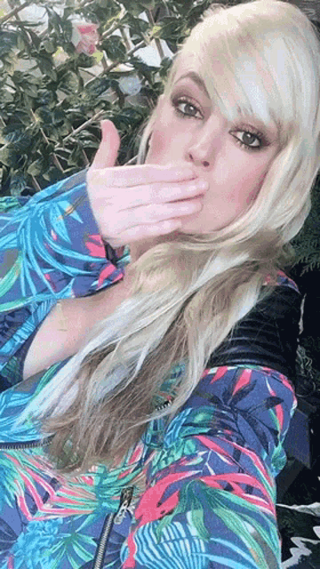a woman covering her mouth with her hand while wearing a blue jacket
