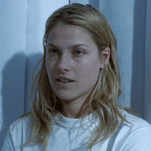 a woman with long blonde hair wearing a white shirt looks at the camera
