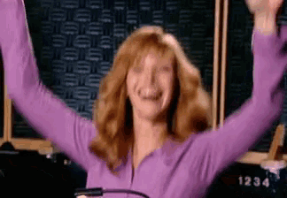 a woman in a purple sweater is raising her arms in the air .