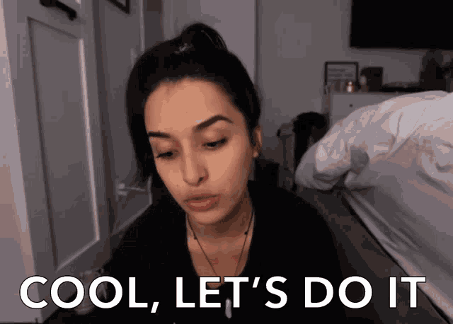 a woman says cool let 's do it while sitting in front of a bed