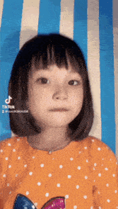 a little girl with short hair is wearing an orange shirt with white polka dots ..