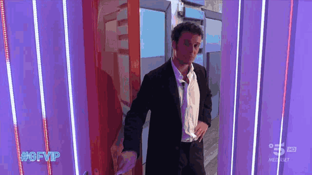 a man in a suit stands in front of a purple wall with #gfvip written on it