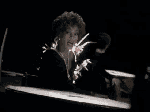 a woman is sitting at a piano in a dark room holding a flower .