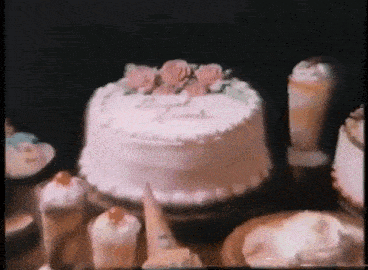 a cake with pink frosting and flowers on top is sitting on a table surrounded by other desserts .
