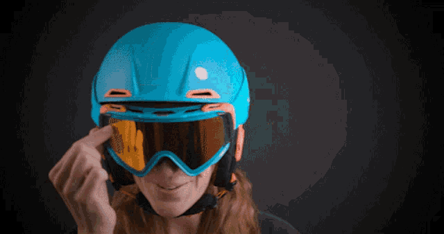 a woman wearing a blue helmet and goggles is smiling