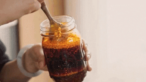 a person is stirring a jar of honey with a spoon .