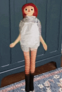 a stuffed doll with red hair and striped legs is standing on a rug .