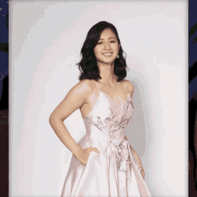 a woman in a pink dress stands with her hands in her pockets and smiles