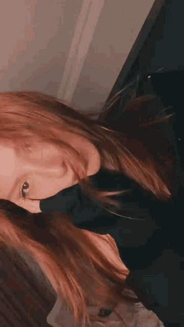 a woman with long red hair is taking a selfie with her hair blowing in the wind