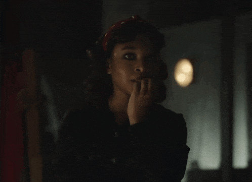a woman with a red headband is smiling and biting her nails in a dark room