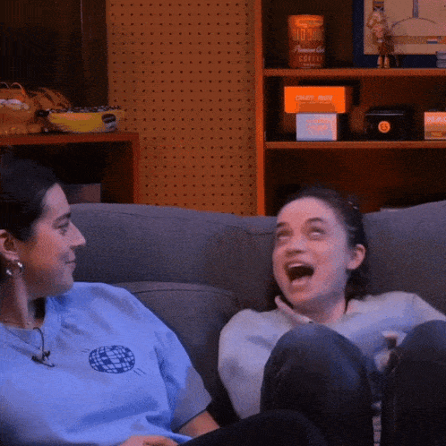 two women are sitting on a couch and one of them is wearing a blue shirt that says globe