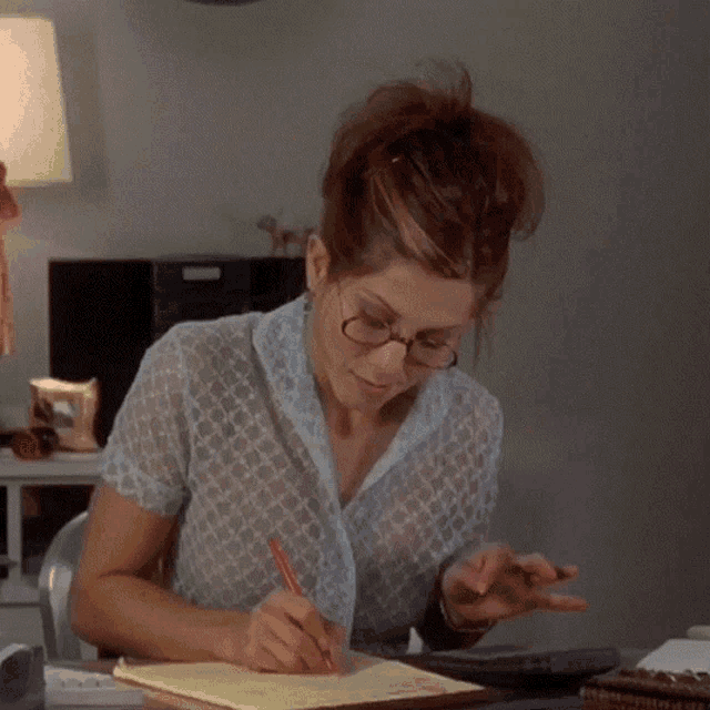 a woman wearing glasses and a sheer shirt is writing in a notebook
