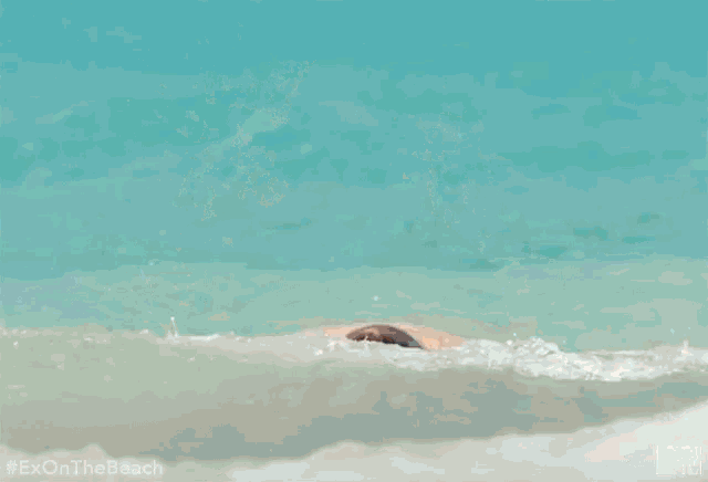 a man is splashed by a wave on the beach and his face is covered in water .