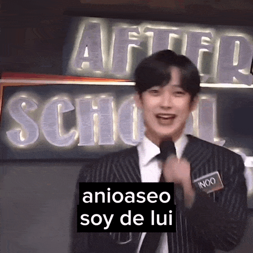 a man in a suit and tie is speaking into a microphone in front of a sign that says after school