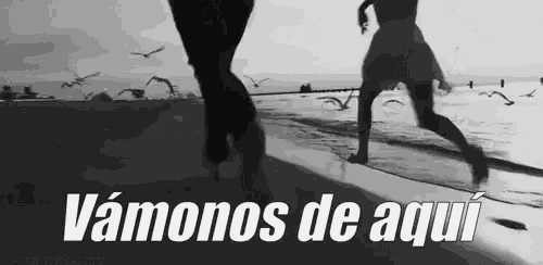a black and white photo of two people running on a beach with the words vamonos de aqui above them