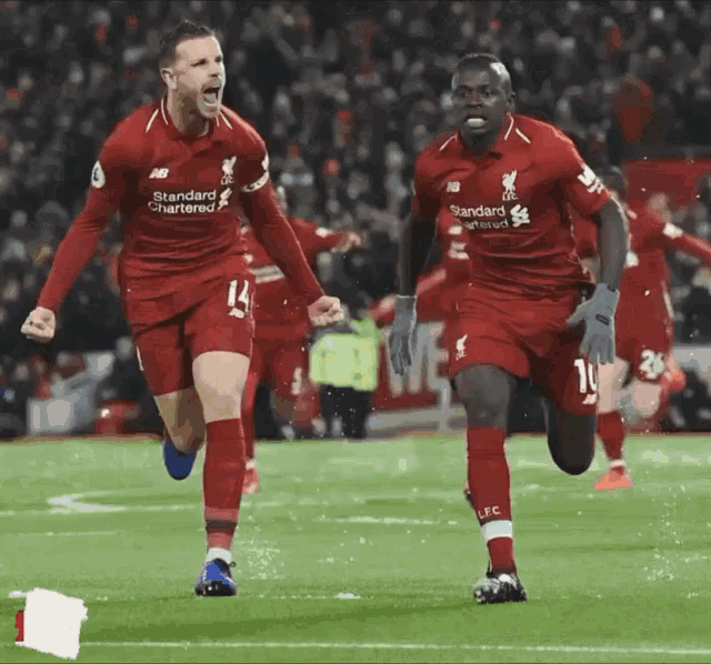 two soccer players wearing red jerseys that say standard chartered on them