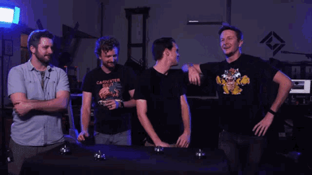 four men are standing around a table and one of them is wearing a shirt that says " carpenter soul "