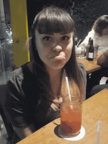 a woman sitting at a table with a drink in front of her and a bottle of beer