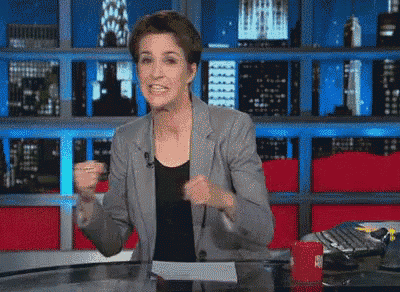 a woman in a gray jacket is standing in front of a microphone in a newsroom .