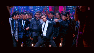a man in a suit and tie is dancing in front of a crowd of men