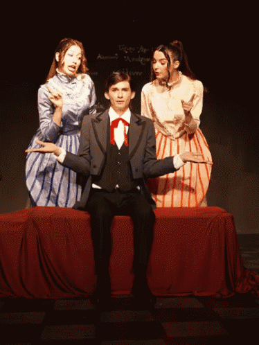 a man in a suit sits on a bench with two women behind him