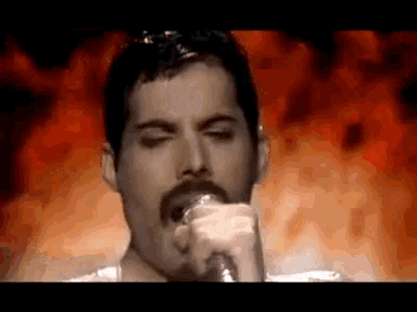 a man with a mustache is singing into a microphone in front of a fire background .