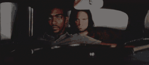 two men are sitting in the back seat of a car looking out the window .