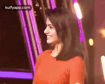 a woman in a red dress is smiling and standing in front of a purple background .