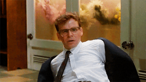 a man wearing glasses and a white shirt is sitting in a chair with his jacket on his back .