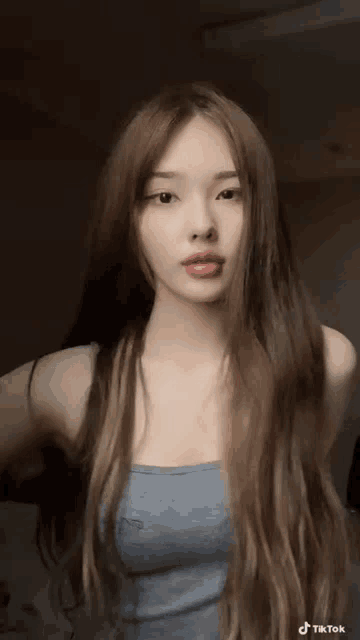 a woman with long brown hair is wearing a blue tank top and making a funny face .