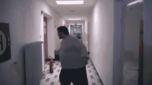 a man is walking down a hallway with a fire extinguisher in the background .