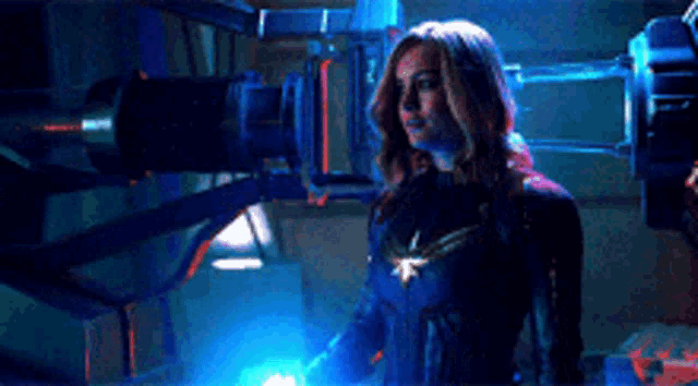 a woman in a superhero costume is standing in a dark room with a blue light behind her .