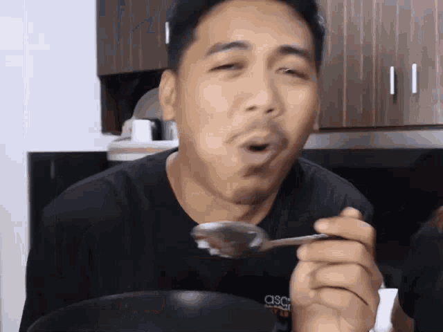 a man wearing a black shirt that says asco on it is holding a spoon