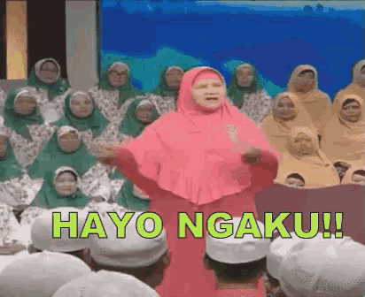 a woman in a pink hijab is standing in front of a crowd of people and says hayo ngaku !!