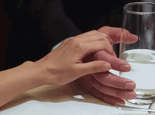 a man and woman holding hands over a glass of water on a table