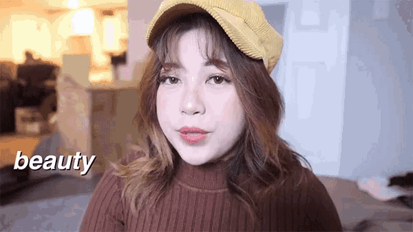 a woman wearing a yellow hat and a brown sweater with the word beauty behind her