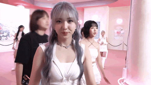 a girl with gray hair is standing in a pink room with other girls